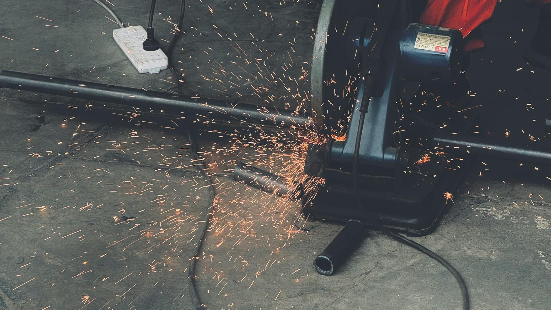A worker using an angle grinder generating vibrant sparks indoors on a concrete floor.
